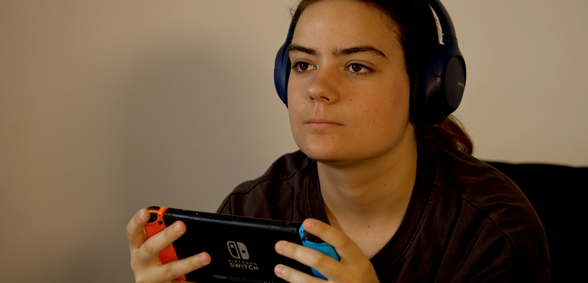 Personne portant un casque audio bleu, concentrée sur un jeu vidéo en tenant une Nintendo Switch.