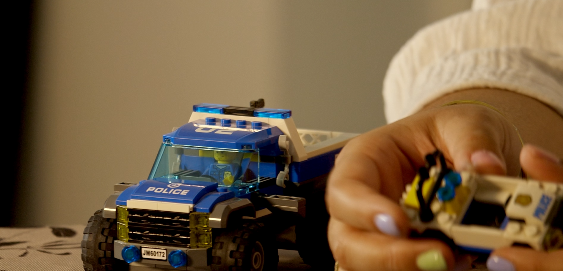 Main d'une personne tenant une petite voiture LEGO, à côté d'un camion de police LEGO avec une figurine de policier à l'intérieur.