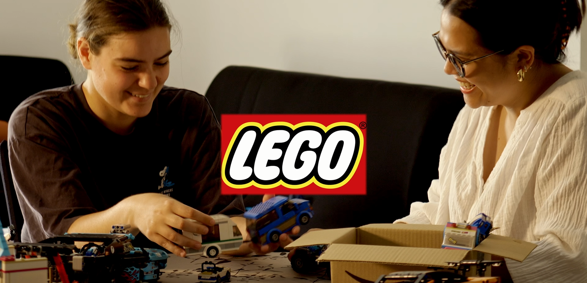 Deux personnes souriantes construisant avec des blocs LEGO, un logo LEGO est affiché au centre de l'image.